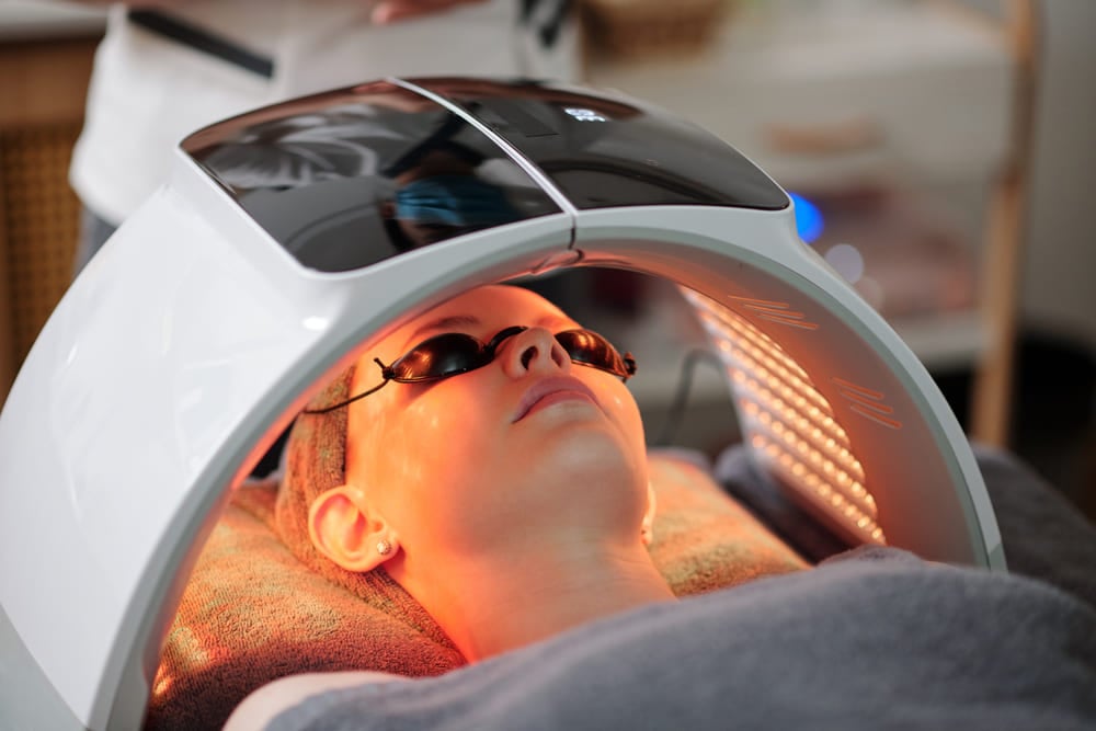 A close-up of a person lying down and receiving a professional LED light therapy treatment.
