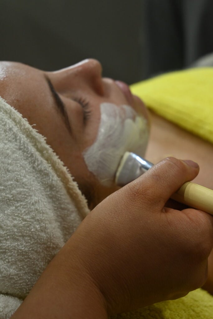 A person lying down with their eyes closed, receiving a facial treatment.