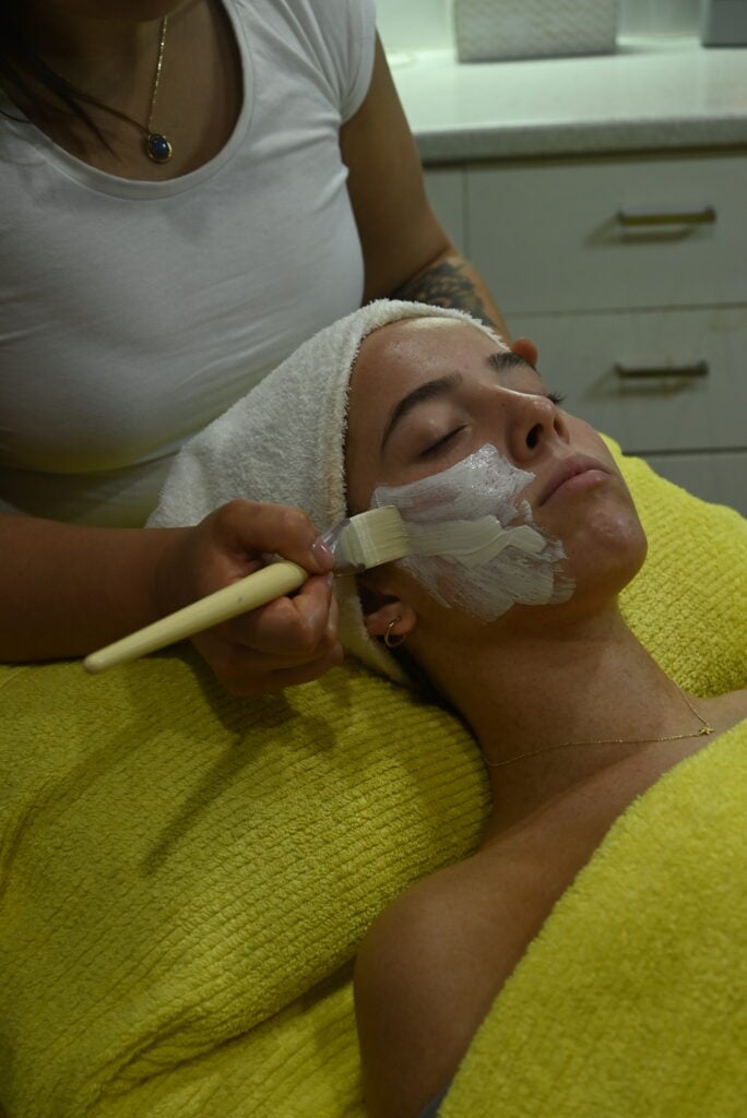 A young woman lying down on a treatment bed, eyes closed, and draped in bright yellow towels.
