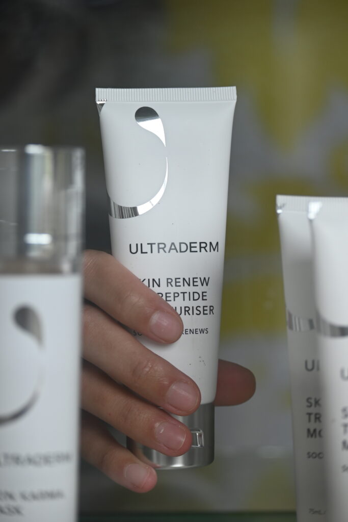 A person's hand holding a white squeeze tube of Ultratherm skincare product.