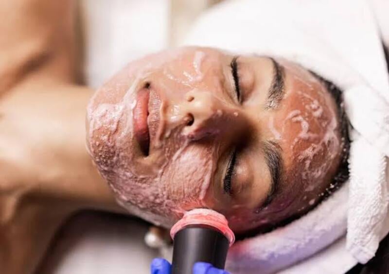 A person with dark hair, lying down with their eyes closed, receiving a high-tech facial treatment.