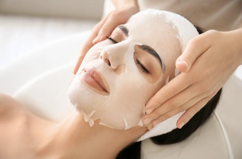 A young woman lying on a spa bed with her eyes closed, receiving a facial treatment.