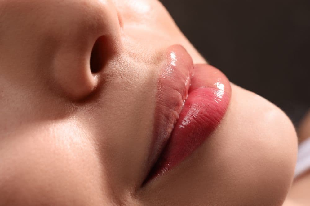 A person's mouth and nose, focusing on the lips which are plumped and glossy with a rich, rosy-pink or berry-colored tint.