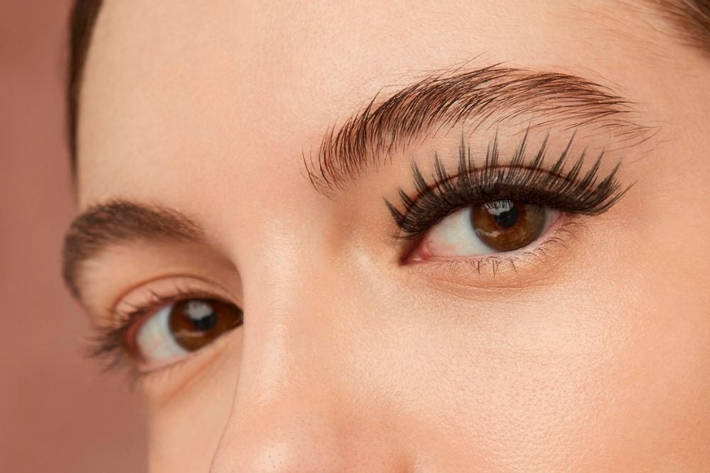 A woman's brown eyes, showcasing a dramatic set of long, voluminous, stylized false eyelashes on the upper lash line.